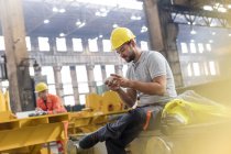 Steel worker texting with cell phone taking a break in factory — Stock Photo