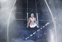 Focused male gymnast performing on gymnastics rings in arena — Stock Photo