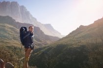 Молодий чоловік з рюкзаком пішохідний, дивлячись на сонячний вид на гору — стокове фото
