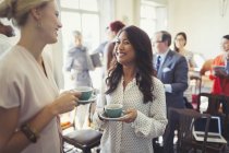 Улыбающиеся деловые женщины, пьющие кофе и работающие в сети на деловой конференции — стоковое фото