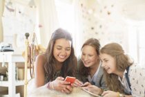 Три дівчинки-підлітки використовують смартфон разом, лежачи на ліжку в спальні — стокове фото