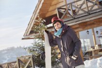 Lächelnde Snowboarderin mit Snowboard vor sonniger Hütte — Stockfoto