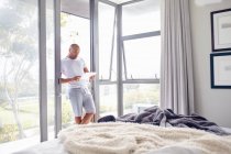 Человек, использующий цифровой планшет в окне спальни — стоковое фото
