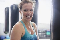 Портрет сміється жінка-боксер стоїть на ударній сумці в спортзалі — стокове фото