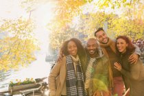 Portrait smiling friends hugging at sunny autumn canal — Stock Photo