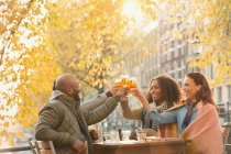 Улыбающиеся друзья пьют бокалы пива в осеннем кафе на тротуаре — стоковое фото
