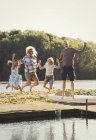 Retrato juguetón familia saltando en el muelle del lago soleado - foto de stock