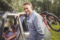 Retrato sonriente padre apoyado en el coche con bicicletas de montaña - foto de stock