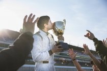 Formula one racing team cheering around driver kissing trophy, celebrating victory — Stock Photo