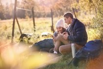 Giovani escursionisti coppia a riposo in erba soleggiata utilizzando il telefono cellulare e tablet digitale — Foto stock