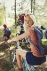 Portrait smiling mother with backpack mountain biking with family in woods — Stock Photo