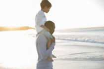 Отец носит сына на плечах на пляже — стоковое фото