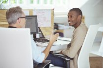 Men sitting at desk in office,talking and smiling — Stock Photo