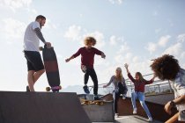 Amigos patinaje en el parque de skate soleado - foto de stock