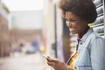Vista lateral de la mujer negra feliz usando el teléfono inteligente - foto de stock