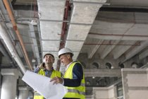 Инженеры-мужчины с фонариком и чертежами на строительной площадке — стоковое фото