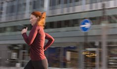 Corredor feminino correndo ao longo do edifício urbano — Fotografia de Stock