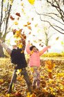 Verspielte Schwestern werfen Herbstblätter in sonnigen Wäldern — Stockfoto