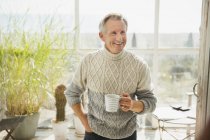 Smiling mature man drinking coffee on sunny beach house sun porch — Stock Photo