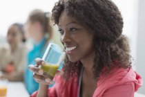Donna sorridente che beve frullato verde sano nel caffè dopo l'allenamento — Foto stock