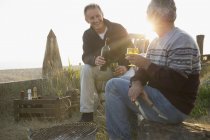 Старші чоловіки п'ють вино і барбекю на пляжі заходу сонця — стокове фото