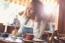 Pensive young woman writing postcard at cafe table — Stock Photo