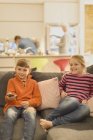 Brother and sister watching TV on living room sofa — Stock Photo