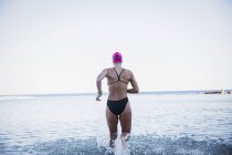 Vista trasera de nadadoras activas femeninas que corren al aire libre en el océano - foto de stock