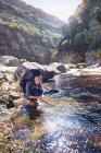 Giovane donna con zaino escursioni, lavarsi le mani al ruscello soleggiato — Foto stock