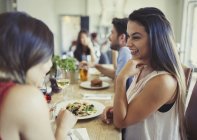 Mulheres sorridentes amigos conversando e comendo na mesa do restaurante — Fotografia de Stock