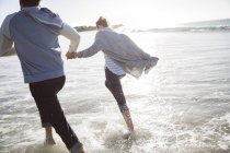 Молодая пара держится за руки и бегает по пляжу — стоковое фото