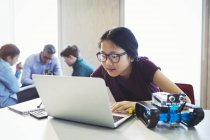Сосредоточенная девочка-студентка программирует робототехнику на ноутбуке в классе — стоковое фото