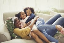 Madre e hijas juguetonas abrazándose en el sofá - foto de stock