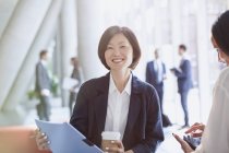 Porträt lächelnde Geschäftsfrau trinkt Kaffee und überprüft Papierkram in Büro-Lobby — Stockfoto