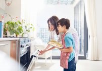 Mother and son baking, placing cookies in oven in kitchen — Stock Photo