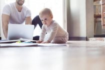 Bambina che gioca sul pavimento vicino al padre che lavora al computer portatile — Foto stock