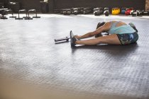 Mujer joven estirándose, haciendo doblez hacia adelante usando barra de pesas en el gimnasio - foto de stock