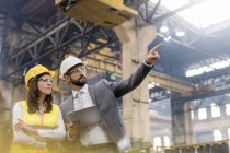 Manager and female steel worker talking looking away in factory — Stock Photo