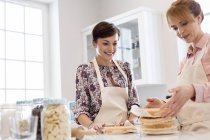 Female caterers baking layer cake in kitchen — Stock Photo