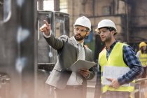 Manager and steel worker talking and looking away in factory — Stock Photo