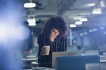Empresária trabalhando até tarde no laptop, bebendo café no escritório escuro — Fotografia de Stock