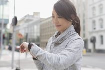 Smiling female runner checking wristwatch on urban sidewalk — Stock Photo