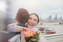 Felice, donna grata che riceve mazzo di fiori, abbracciando fidanzato sul lungomare urbano — Foto stock
