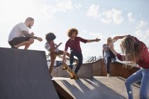 Жінка фотографує друзів-чоловіків скейтбординг на пандусі в сонячному скейт-парку — стокове фото