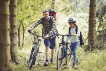 Pai e filha com mochilas caminhando bicicletas de montanha na floresta — Fotografia de Stock