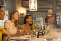 Smiling women friends looking away dining and drinking white wine at restaurant table — Stock Photo