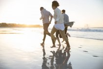 Quatro amigos correndo ob praia ao sol da noite — Fotografia de Stock