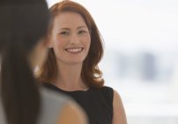 Donna d'affari sorridente con i capelli rossi che parla con un collega — Foto stock