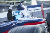 Fórmula de retrato um piloto de carro de corrida usando capacete e torcendo com punho na pista de esportes — Fotografia de Stock