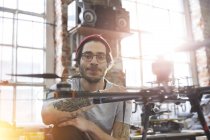 Portrait confident male designer with tattoos working on drone in workshop — Stock Photo